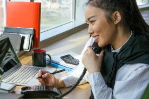 Mulher jovem sorrindo usando notebook em casa, estudando um curso de auxiliar administrativo online com certificado.