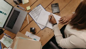 Pessoa estudando em computador com planilhas e documentos, representando um curso para auxiliar administrativo.