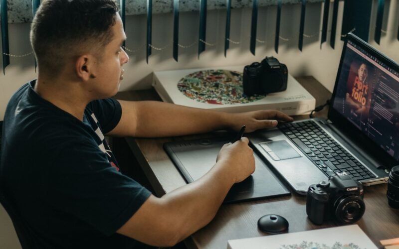 Jovem designer criando um portfólio digital em um computador, com elementos gráficos e ferramentas de design ao redor, simbolizando a construção de um portfólio.
