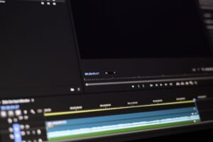 Jovem editor de vídeo freelancer trabalhando em seu laptop, com fones de ouvido e uma interface de software de edição de vídeo na tela, simbolizando trabalho remoto e criatividade.