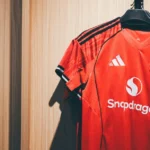 Close-up de uma camisa de futebol com detalhes de costura e escudo, mostrando a qualidade 1.1 tailandesa.