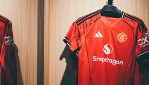 Close-up de uma camisa de futebol com detalhes de costura e escudo, mostrando a qualidade 1.1 tailandesa.