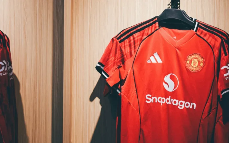Close-up de uma camisa de futebol com detalhes de costura e escudo, mostrando a qualidade 1.1 tailandesa.