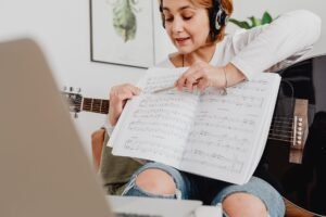 Pessoa tocando violão com um tablet aberto mostrando um curso online em um ambiente acolhedor e bem iluminado.
